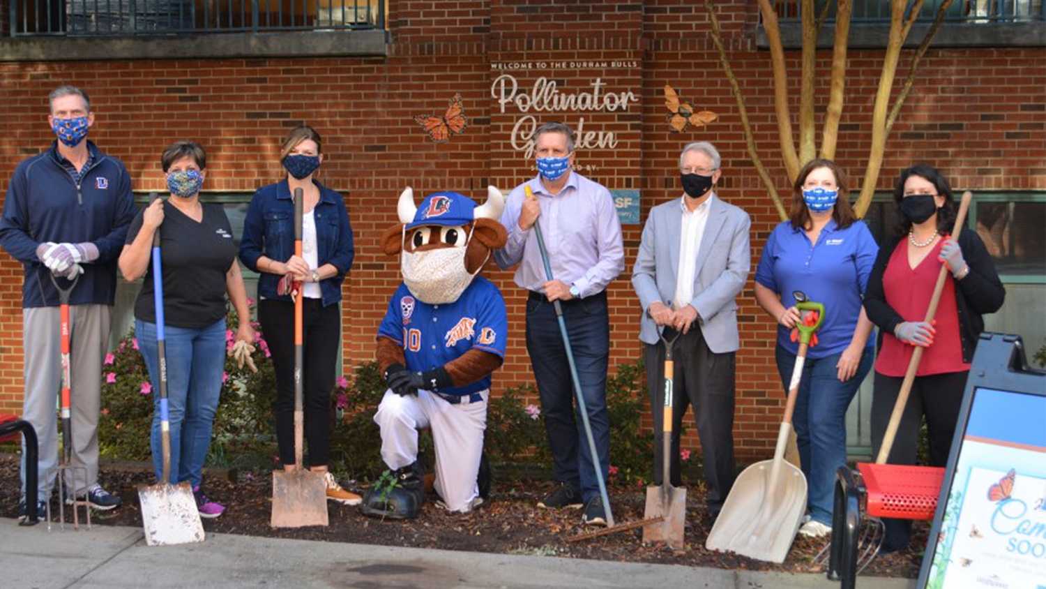 Wolfspeed employees posing with the the Durham Bulls mascot while volunteering to create a Pollinator Garden