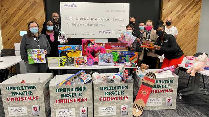 Wolfspeed employees standing around a table full of toys and gifts for children while holding up a large donation check to the Operation Rescue Christmas nonprofit.