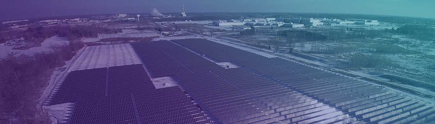 Landscape shot of a solar farm with hundreds of solar panels surrounded by a rural setting in the background.